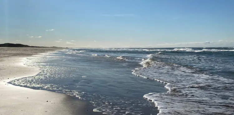 Wellen laufen an einem weiten Sandstrand in Dänemark aus