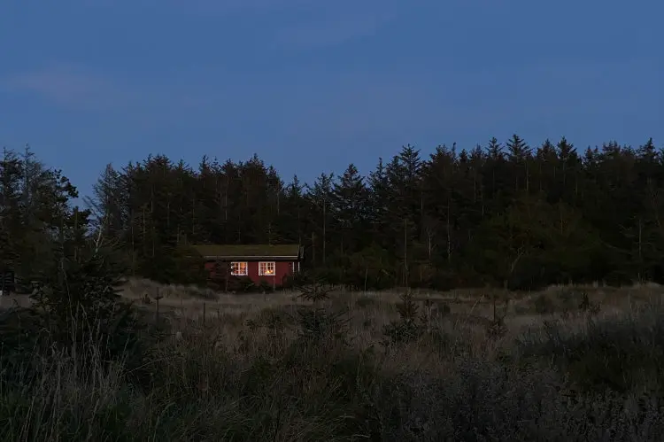 Rotes Holzhaus mit erleuchteten Fenstern in der Abenddämmerung vor dunklem Nadelwald