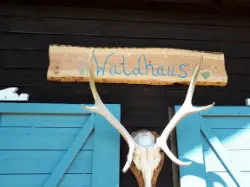Holzschild „Waldhaus“ über türkisfarbenen Türen mit Hirschgeweih