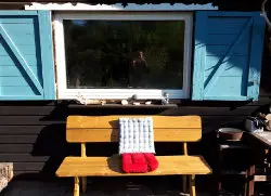 Holzbank mit Kissen vor dem Fenster des Waldhauses mit türkisfarbenen Fensterläden