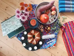 Herbstlicher Ritualtisch mit Kuchen im Kerzenkreis, Kürbis, Äpfeln, Blumen und bunten Tüchern